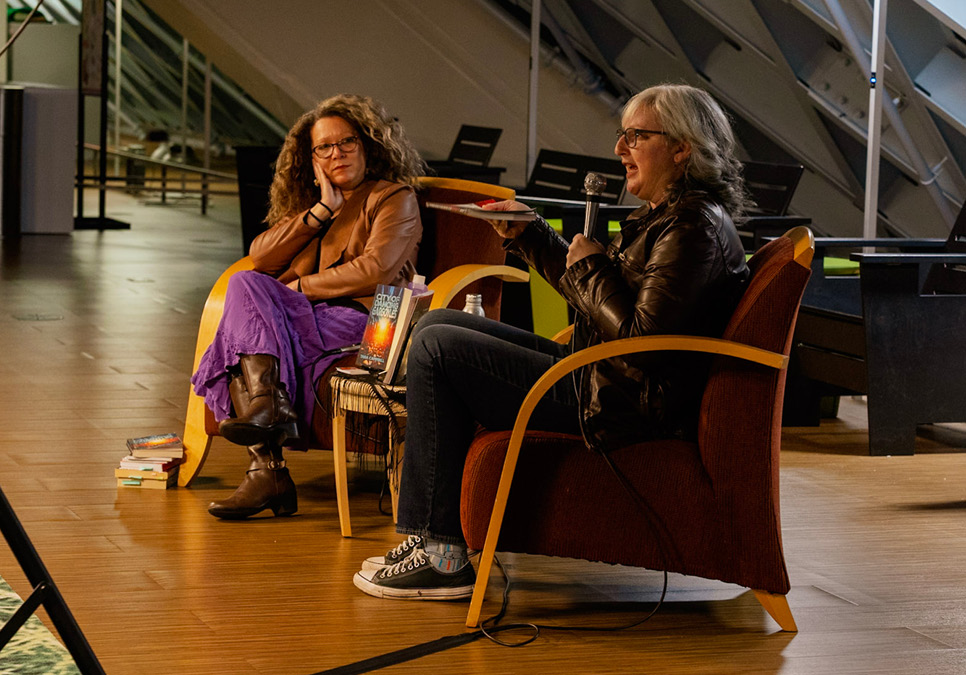 Two people sitting in chairs. One holds a microphone.
